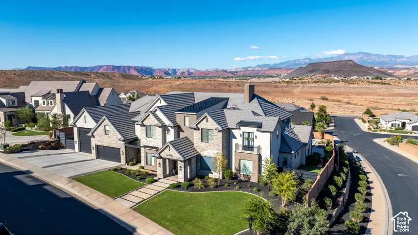 Multi-level residence featuring stone and stucco exterior, dark tile roof, paved driveway, three-car garage, and desert landscape backdrop