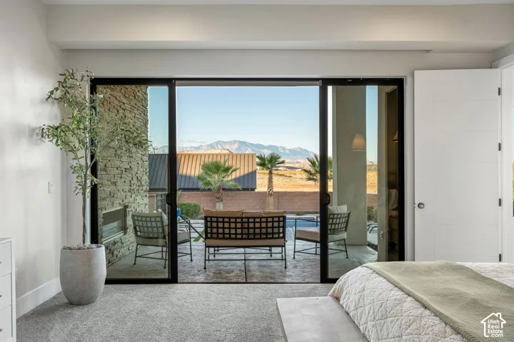 Floor-to-ceiling sliding glass doors, textured stone accent wall, covered patio with stamped concrete flooring, and mountain backdrop