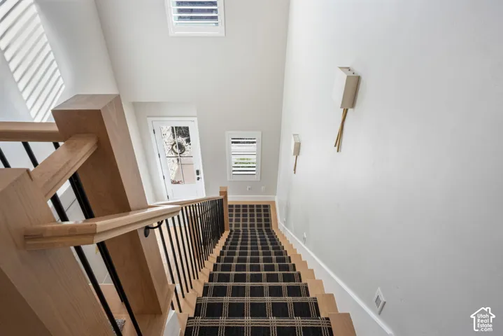 Staircase featuring wood-finish handrails, black vertical balusters, patterned stair runner, and wall-mounted light fixtures