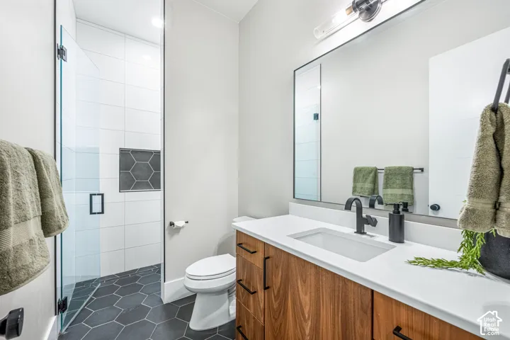 Bathroom featuring a wood-finish vanity with a quartz countertop, matte black fixtures, a walk-in shower with floor-to-ceiling tile, and hexagonal floor tile