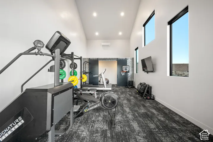 Vaulted ceiling featuring recessed lighting, multi-level windows with black frames, sliding barn-style doors with brick-patterned surround, and wall-mounted climate control unit