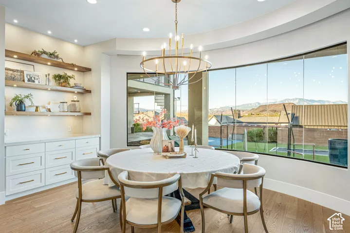 Curved wall of windows, custom built-in white cabinetry with floating wood shelving, recessed lighting, brass-finish tiered chandelier, and wide-plank wood-finish flooring