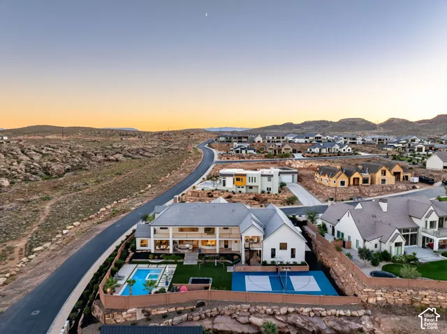 Aerial perspective of a multi-level residence featuring a backyard swimming pool with integrated spa, a paved sports court, manicured lawn, and multi-level balconies