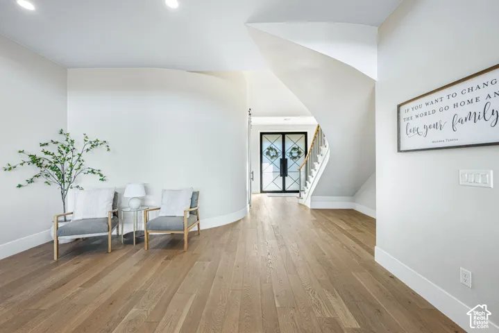 Foyer featuring wood-finish flooring, a curved architectural wall, and a staircase with a metal railing, highlighted by double glass-panel entry doors