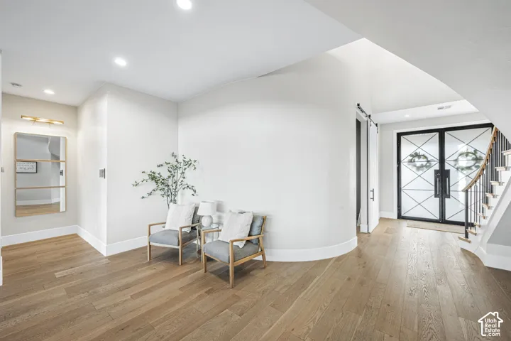 Entry featuring wood-finish flooring, a curved architectural wall, a double-door entryway with geometric glass detailing, a built-in recessed mirror, and a staircase with metal railings