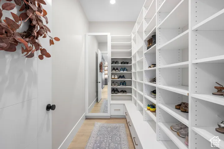 Custom walk-in closet featuring extensive white floor-to-ceiling shelving, built-in storage drawers, integrated full-length mirror, and wood-finish flooring