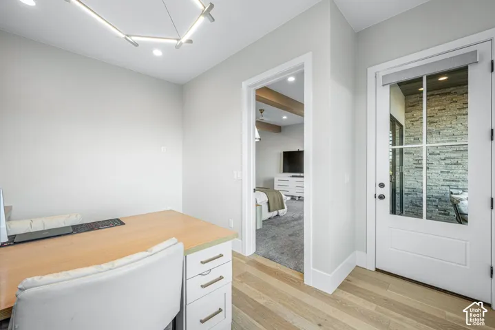 Modern office space featuring wood-finish flooring, a geometric LED chandelier, and a white door with a multi-pane glass insert