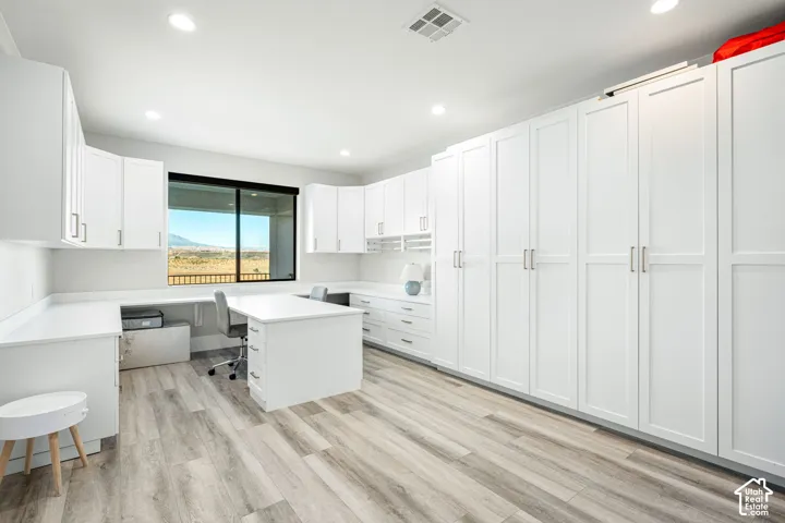 Extensive built-in white cabinetry, integrated desk space with drawers, recessed lighting, wood-finish flooring, and a large window with exterior mountain scenery