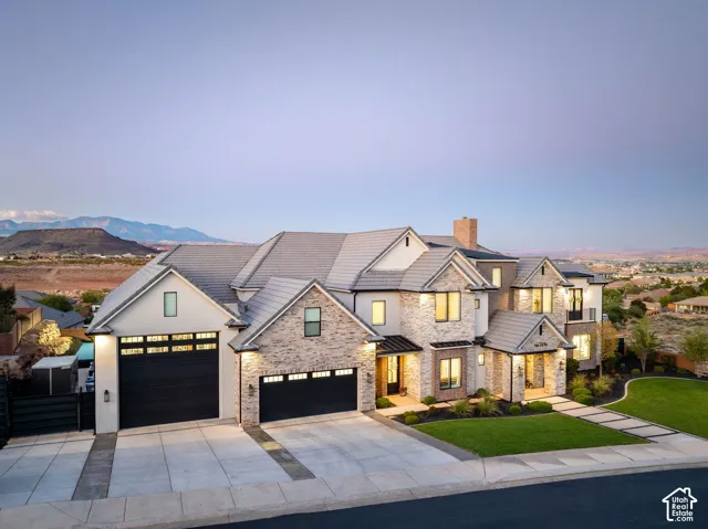 Multi-gabled exterior featuring stone veneer siding, concrete tile roofing, three-car garage, manicured lawn, and mountain backdrop