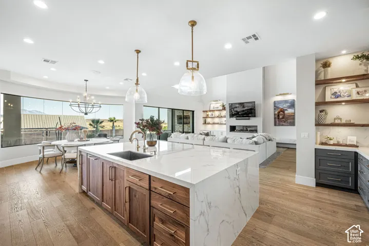 Kitchen featuring a waterfall-edge island with stone-finish countertops, wood-finish cabinetry, recessed lighting, glass pendant fixtures, and wood-finish flooring