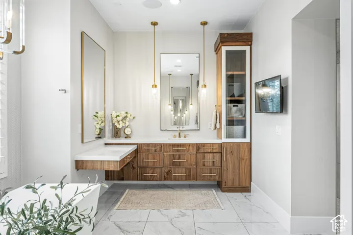 Floating wood-finish vanity with countertop, vertical built-in cabinetry, dual mirrors, brass pendant lighting, and stone-finish flooring