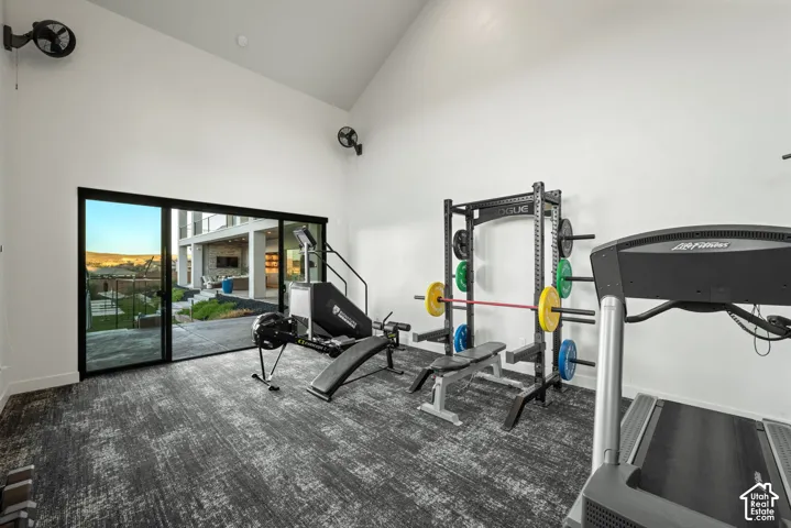 Vaulted ceilings, dark textured carpeting, and wall-mounted fans, featuring a large sliding glass door with exterior access