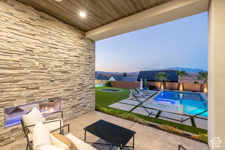 Covered patio featuring a stacked stone accent wall with a linear built-in fireplace, wood-finish ceiling, swimming pool, and concrete hardscaping
