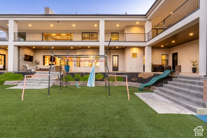 Two-story exterior featuring a covered upper-level balcony with metal railing, recessed exterior lighting, dual-level concrete staircases, and stone masonry siding accents