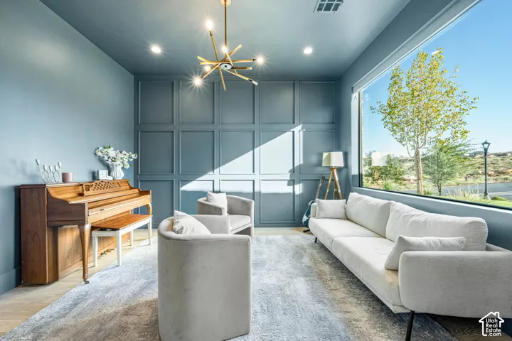 Floor-to-ceiling grid-patterned wainscoting, expansive picture window, modern brass multi-arm chandelier, recessed lighting, and light-tone wood-finish flooring