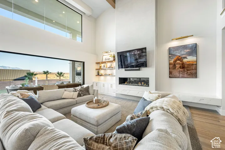 Vaulted ceilings with floor-to-ceiling windows, linear gas fireplace with stone-finish hearth, built-in cabinetry, and wood-finish flooring