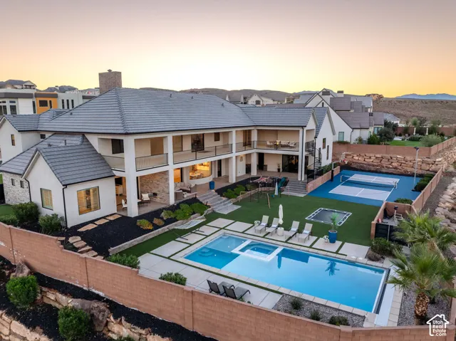 Multi-level exterior featuring a covered patio with stone accents, a built-in swimming pool with an integrated spa, a dedicated pickleball court, and manicured landscaping