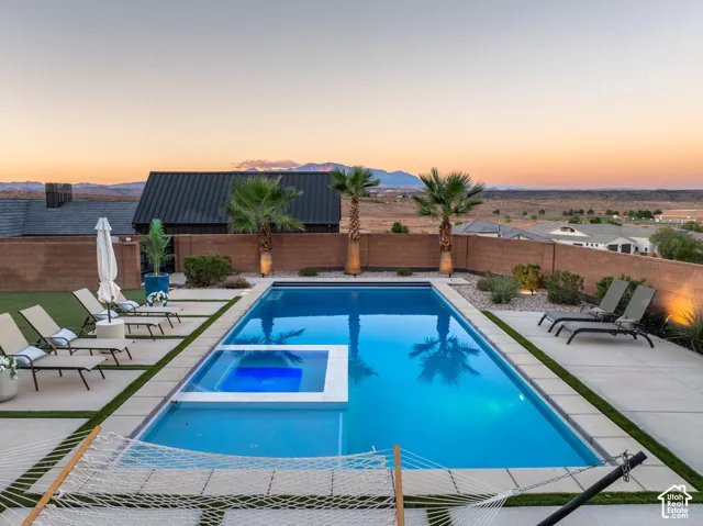 In-ground swimming pool with an integrated spa, expansive concrete patio, synthetic turf lawn, and perimeter masonry wall, set against a mountainous horizon
