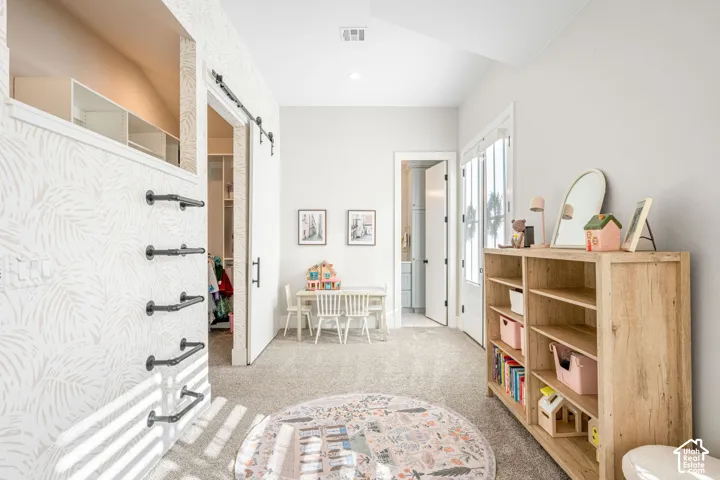 Interior space featuring patterned wallpaper, a black metal sliding barn door, integrated wall-mounted climbing bars, carpeted flooring, and glass-paneled double doors
