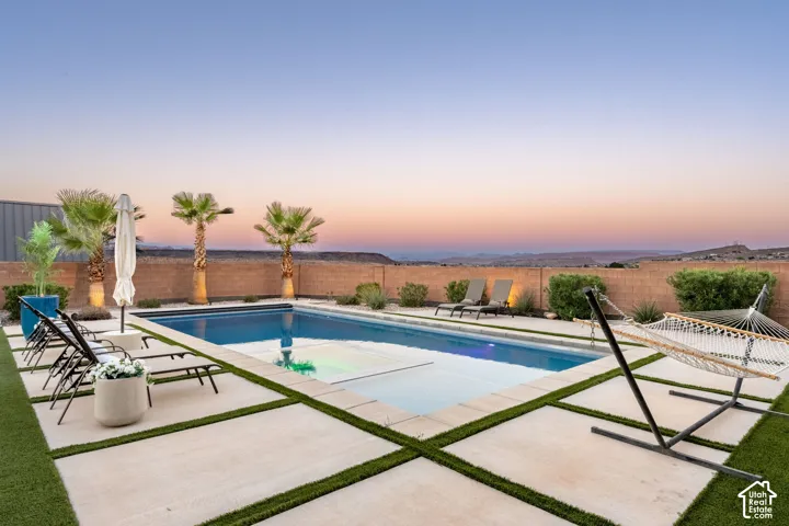 Swimming pool featuring an integrated tanning ledge, expansive concrete paver decking, artificial turf accents, and a masonry perimeter wall set against a mountain backdrop