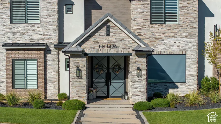 Stacked stone exterior facade featuring a covered entryway, double glass doors with geometric muntin patterns, concrete paver walkway, and integrated wall-mounted exterior lighting