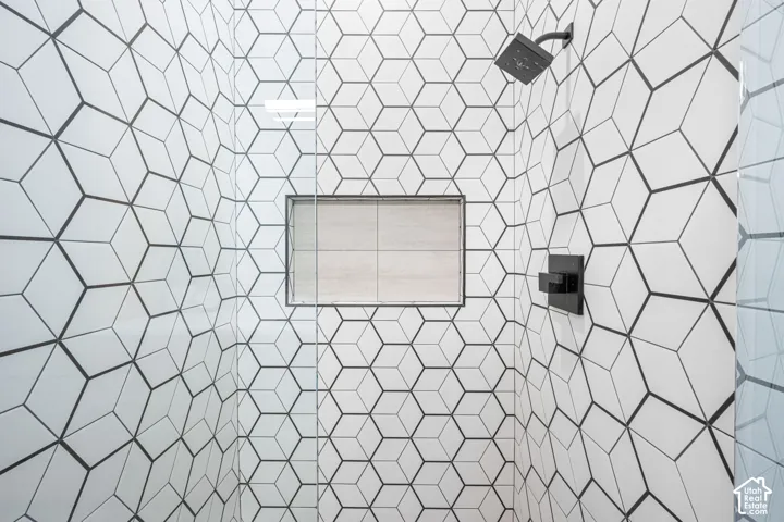 Walk-in shower featuring geometric-patterned wall tile, frameless glass enclosure, recessed wall niche, and matte black plumbing fixtures