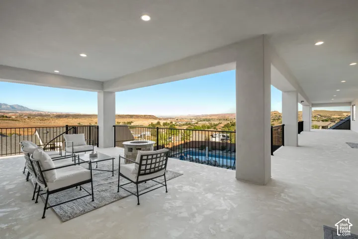 Covered outdoor balcony featuring recessed lighting, a stone fire pit, and black metal railings with panoramic landscape scenery