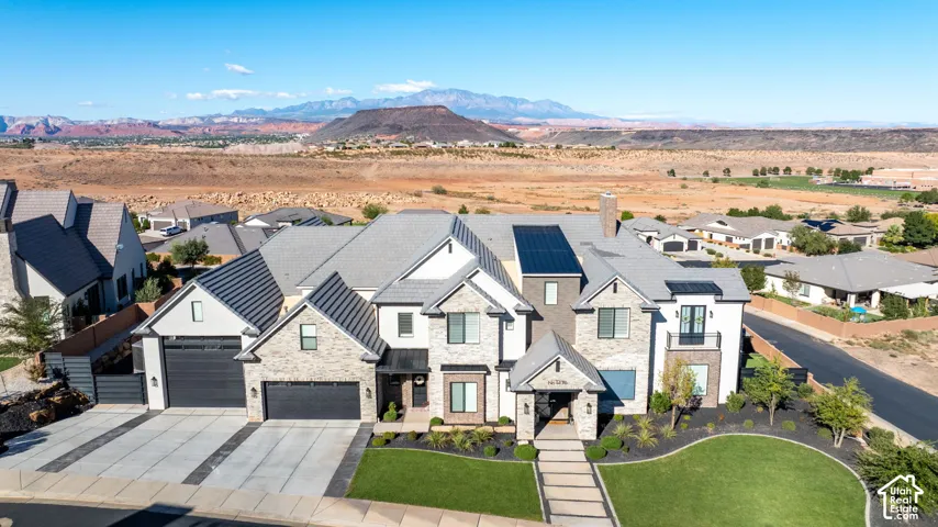 Multi-level exterior featuring light-toned stone and stucco facade, multi-gabled roofline, integrated solar panels, three-car garage, and expansive mountain scenery
