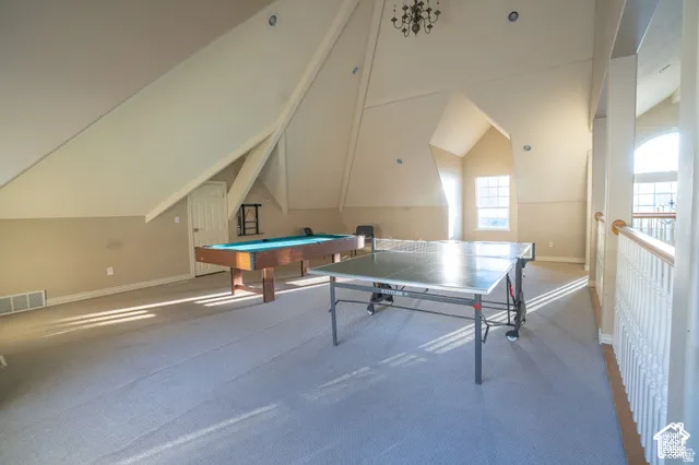 Vaulted ceilings featuring exposed structural beams, wall-to-wall carpeting, multi-pane windows, and a classic wood-spindle banister