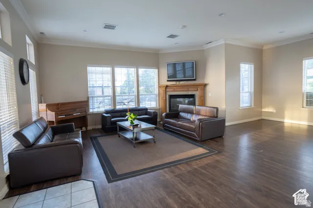 Living area featuring wood-finish flooring, a fireplace with a wood mantle, multi-pane windows, and crown molding