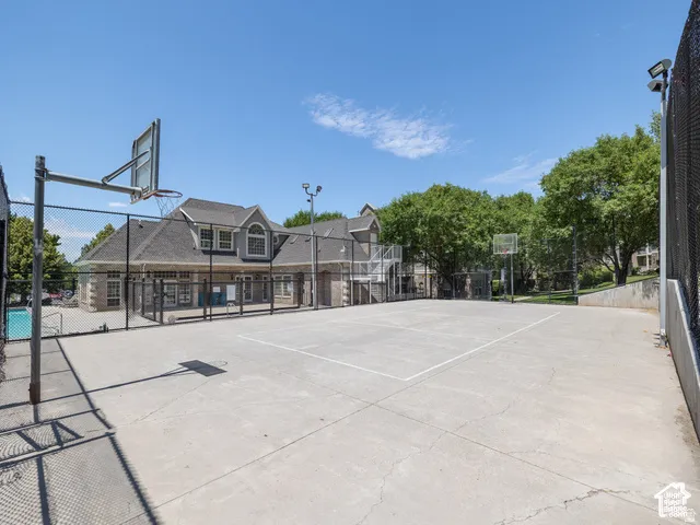 Outdoor recreational area featuring a concrete basketball court, perimeter chain-link fencing, and elevated pole lighting