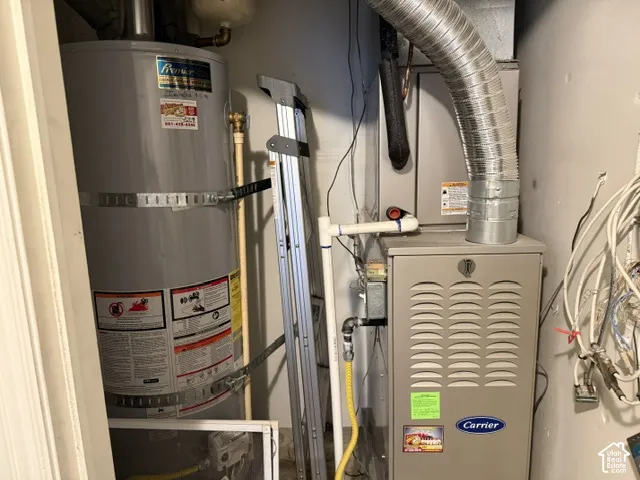 Utility area featuring a water heater and a Carrier forced-air furnace with metal ductwork