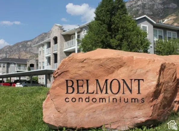 Multi-story condominium exterior featuring light-toned masonry, private balconies, covered parking, and mountain scenery