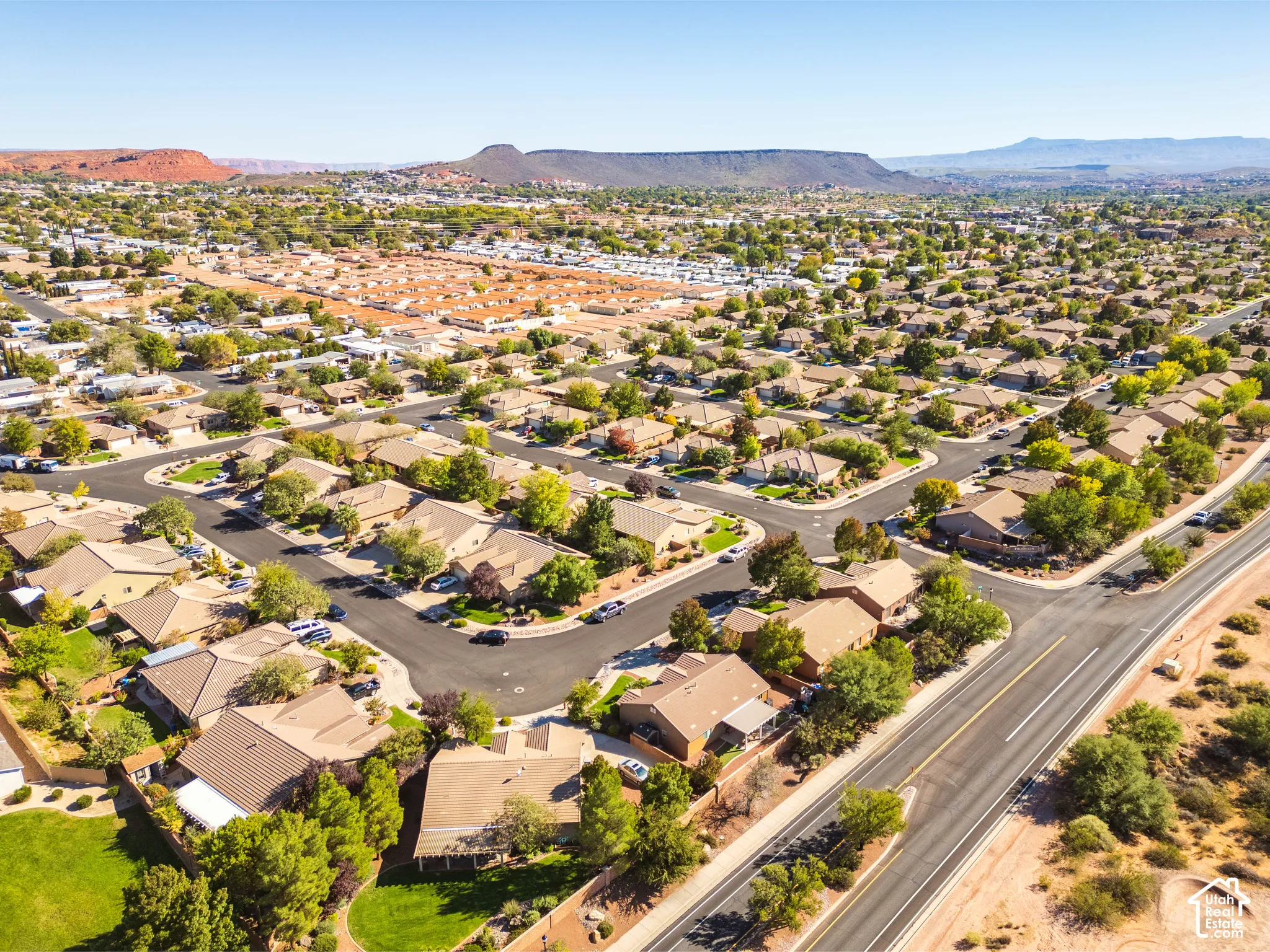 Aerial perspective of residential neighborhood featuring paved streets, mature trees, manicured lawns, and desert mountain backdrop