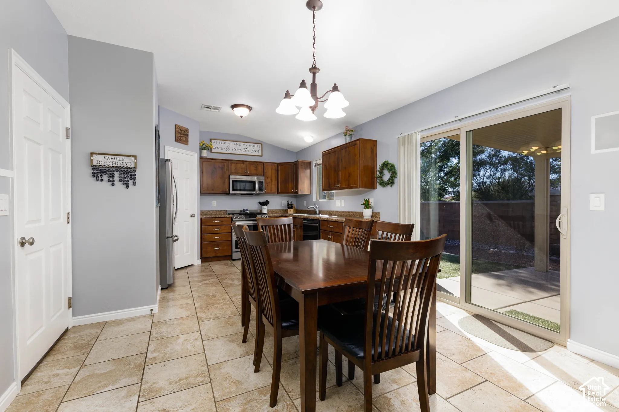 Kitchen featuring wood cabinetry, stone-style tile flooring, stainless steel appliances, and a sliding glass door providing exterior access
