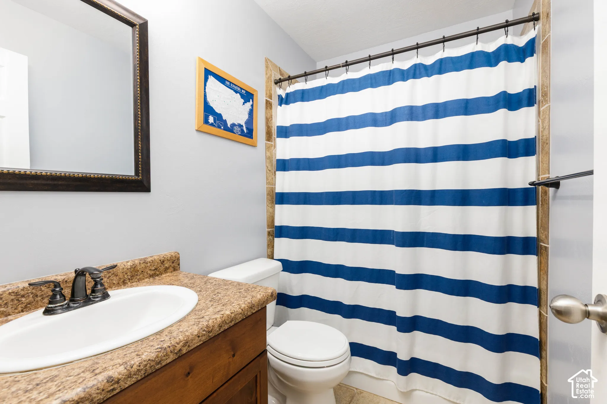 Bathroom featuring a vanity with a stone-finish countertop, an integrated oval sink with a dark-finish faucet, a framed wall mirror, and tile shower surround