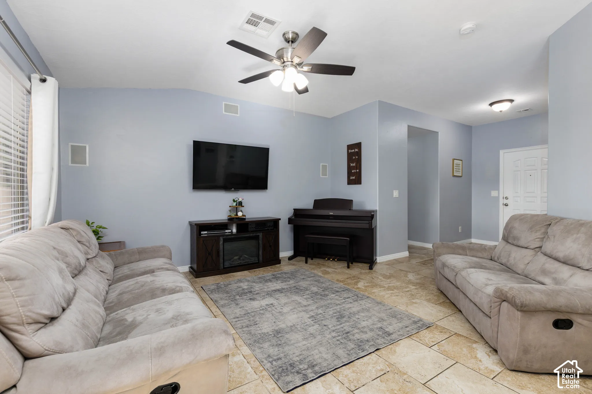 Living area featuring neutral-tone stone tile flooring, vaulted ceilings, and a central brushed-metal ceiling fan with integrated lighting