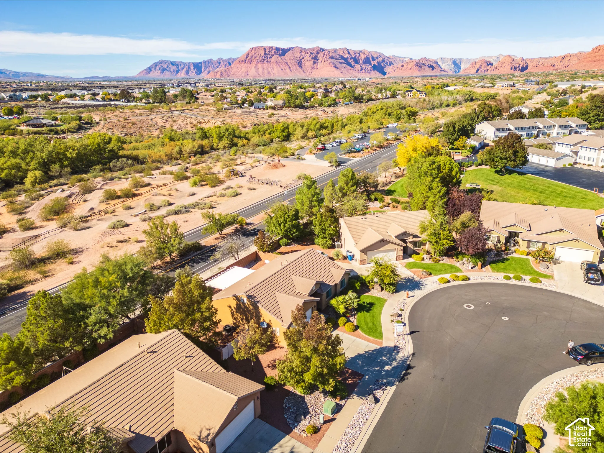 Aerial perspective of residential property featuring a tile roof, paved driveway, landscaped grounds with mature trees, and prominent mountain backdrop