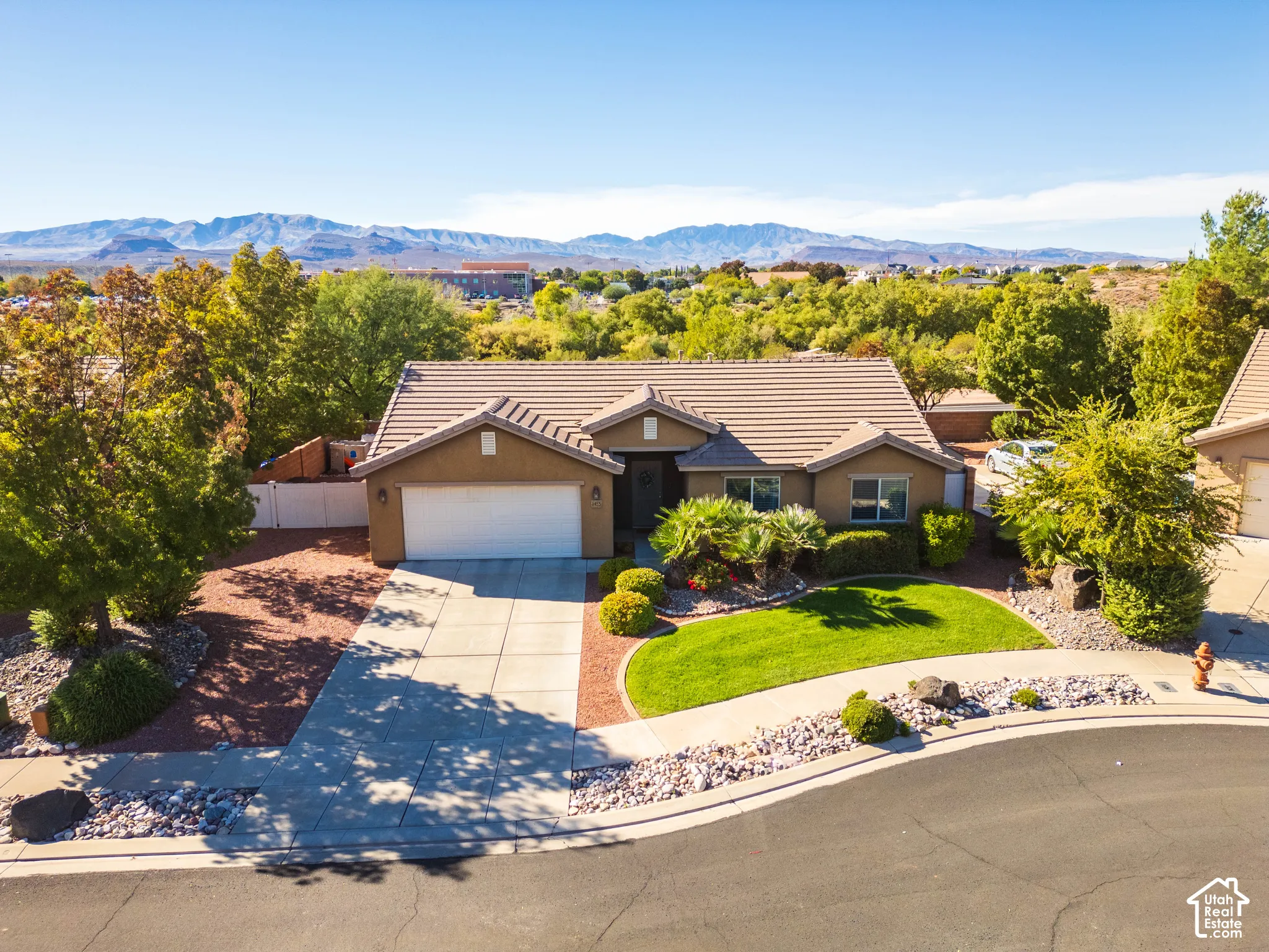 Single-story residence featuring a tile roof, two-car garage, manicured lawn, xeriscaped front yard, and a prominent mountain backdrop