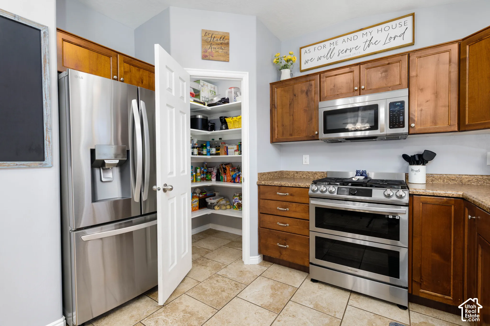 Kitchen featuring stained wood cabinetry, stainless steel appliances, stone-finish countertops, tiled flooring, and a walk-in pantry