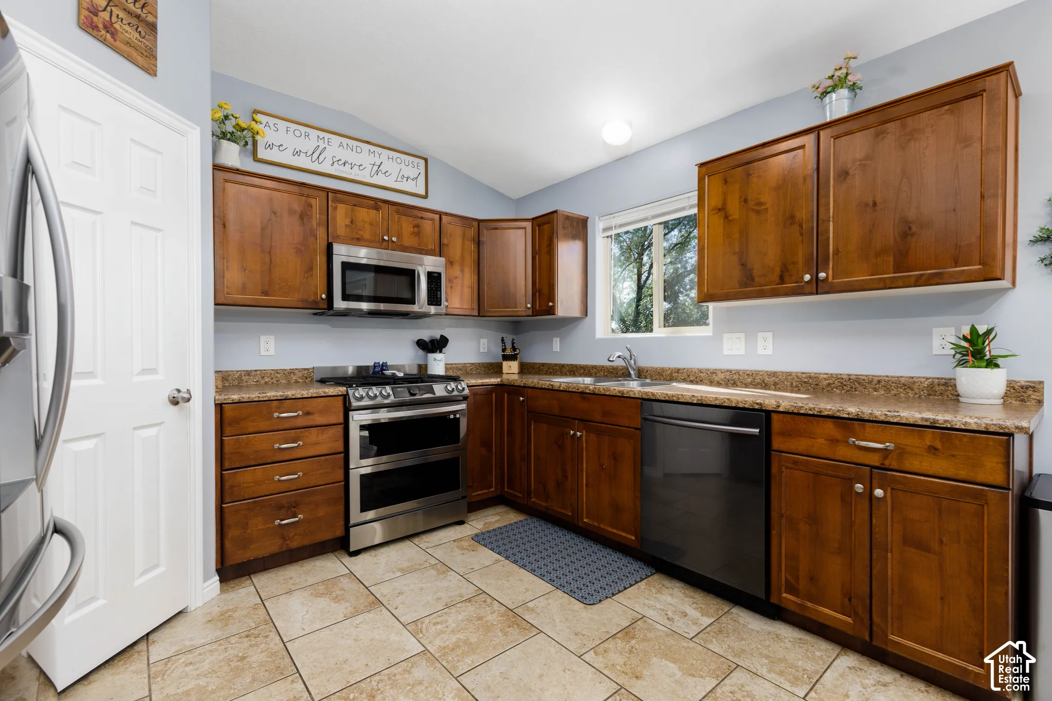 Kitchen featuring stained wood cabinetry, stone-finish countertops, stainless steel appliances, and ceramic tile flooring