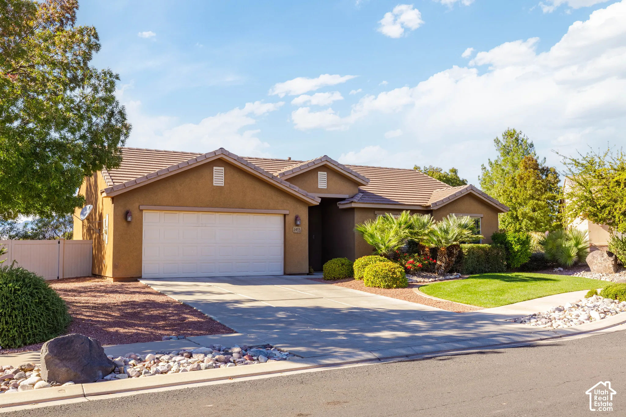 Stucco exterior featuring a concrete tile roof, two-car garage, concrete driveway, and landscaped front yard with rock ground cover