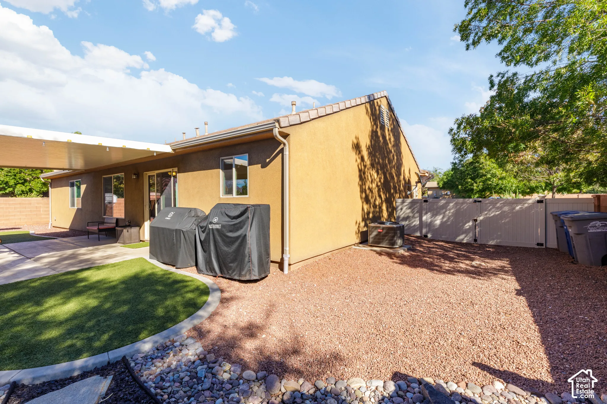 Stucco exterior featuring a covered patio, synthetic turf lawn, stone-mulched ground cover, and a vinyl perimeter privacy fence