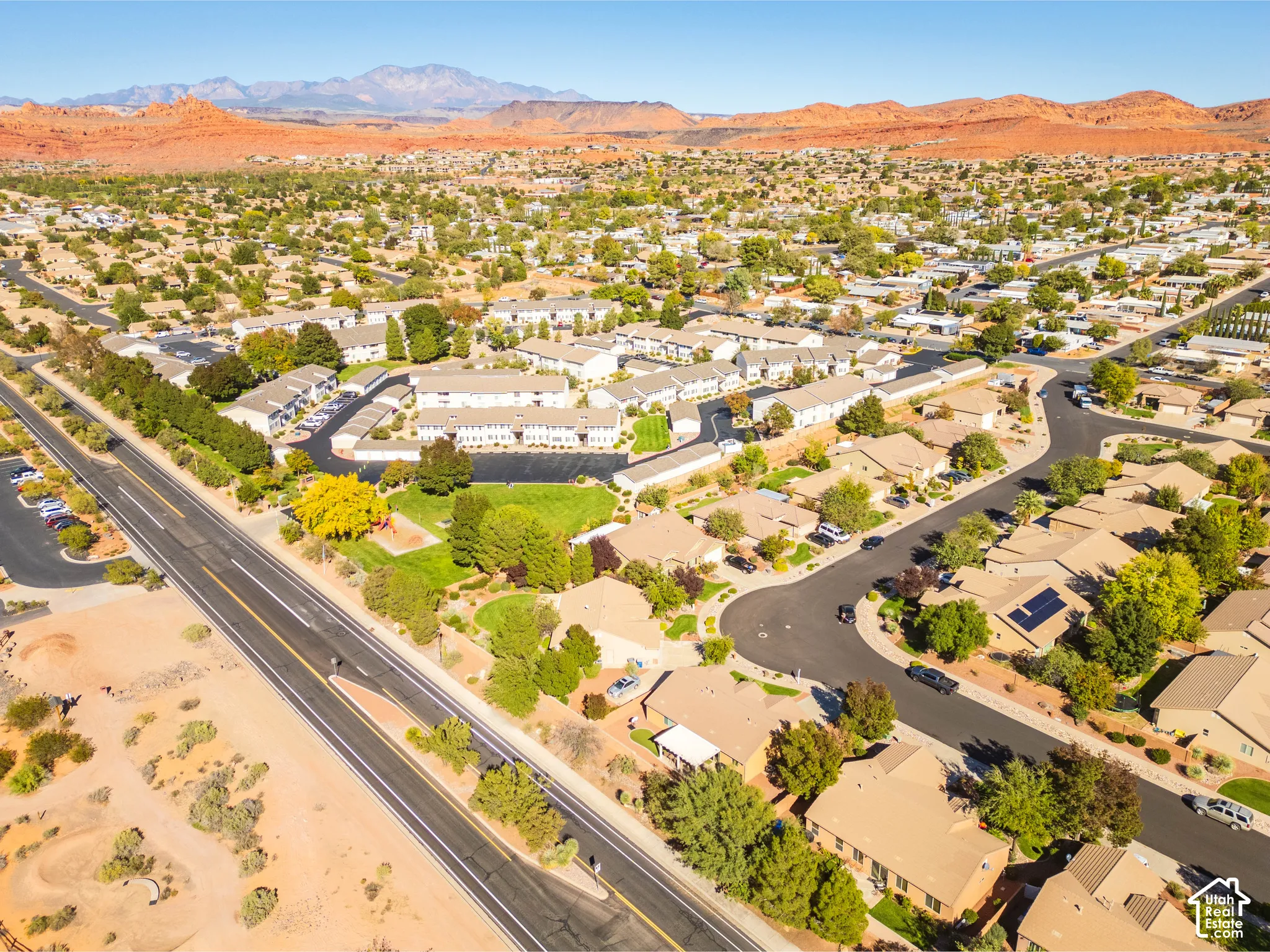Aerial perspective featuring desert landscape, red rock mountain backdrop, and mature tree canopy throughout the residential community