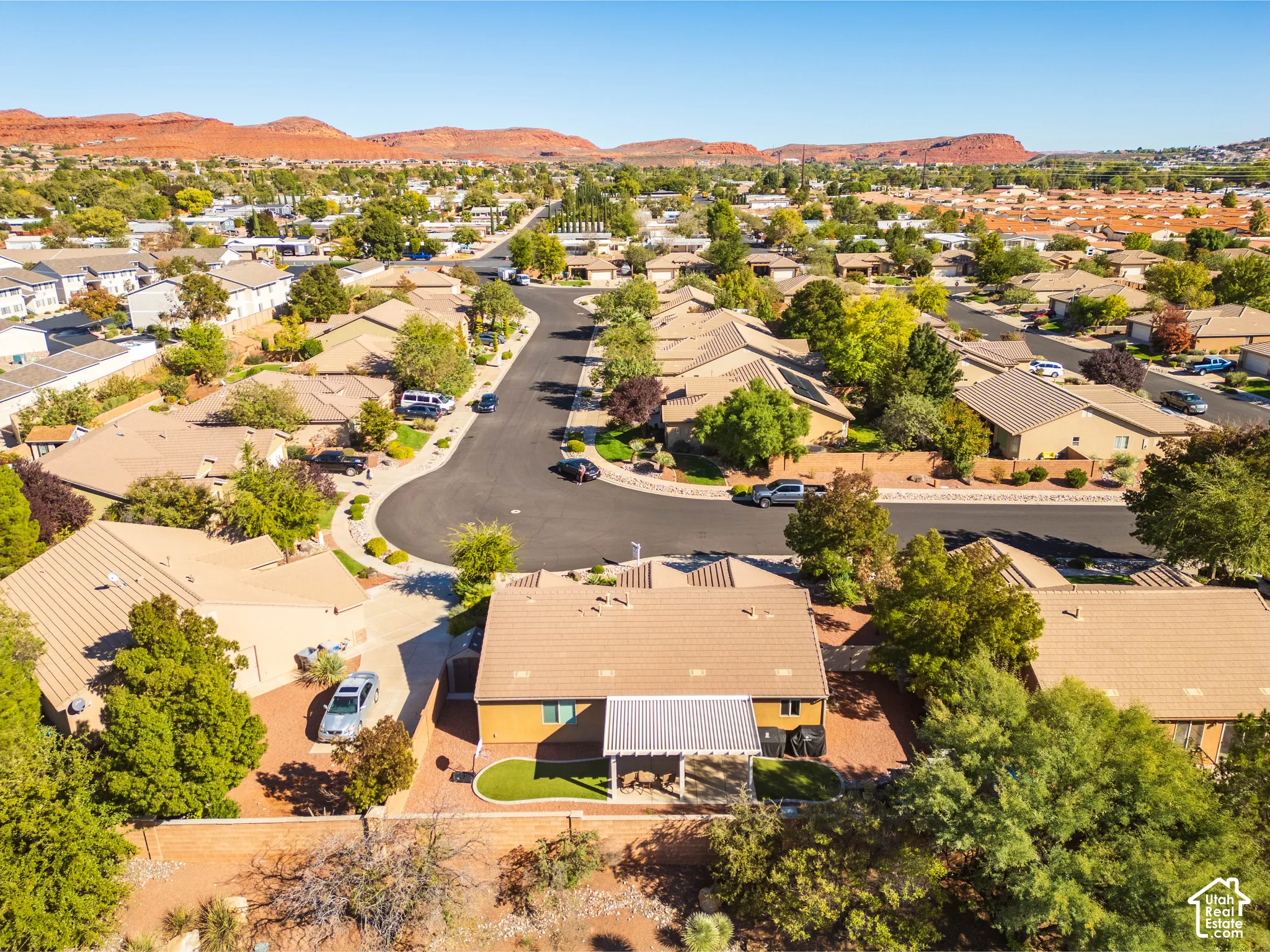 Aerial perspective featuring a single-story residence with a tile roof, a covered rear patio, a fenced lot, and a backdrop of red rock formations