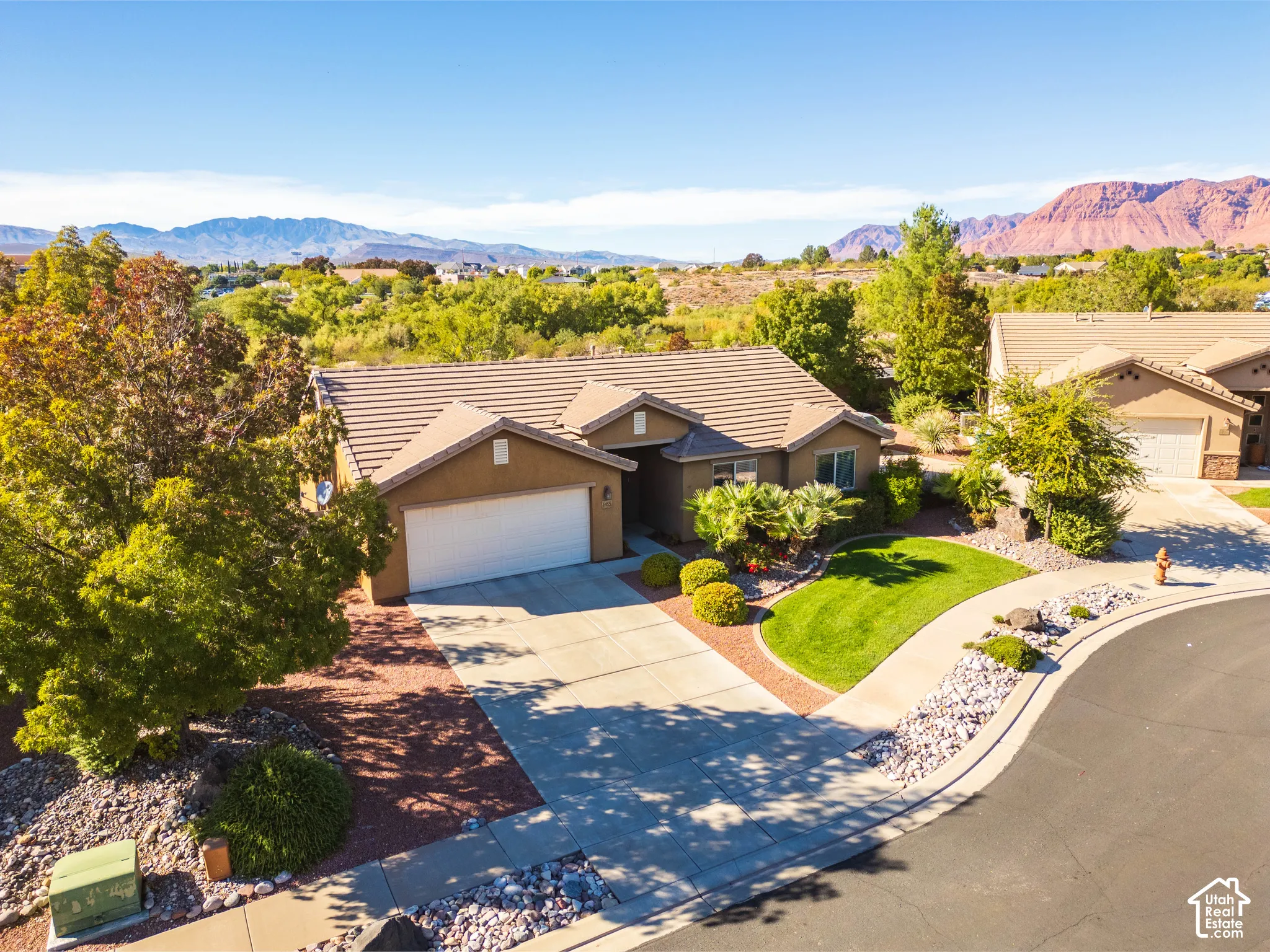 Stucco exterior featuring a tiled roof, multi-car garage, concrete driveway, and manicured landscaping set against a mountain backdrop
