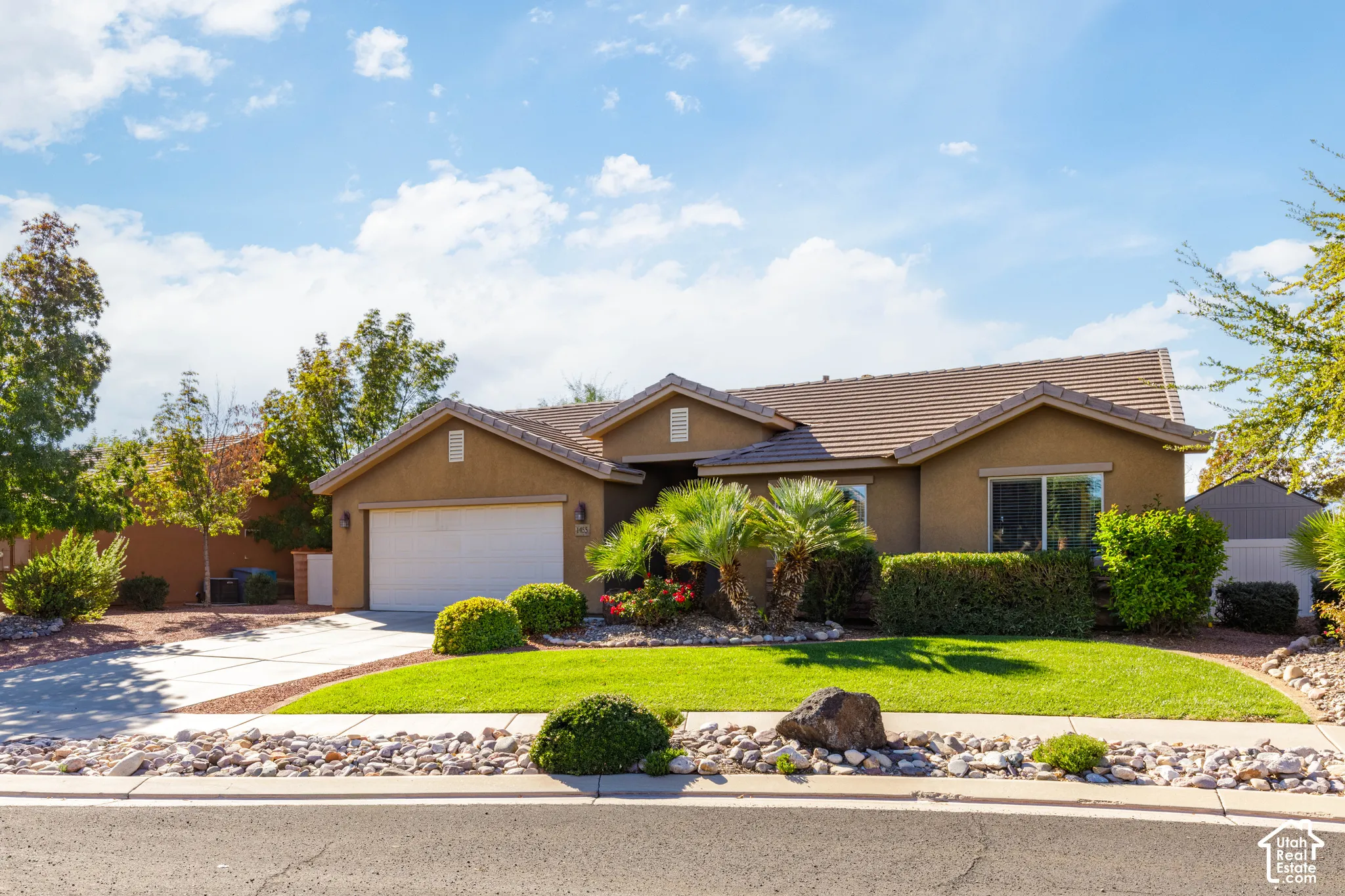 Single-story stucco exterior featuring a concrete tile roof, two-car garage, manicured lawn, and stone-accented desert landscaping