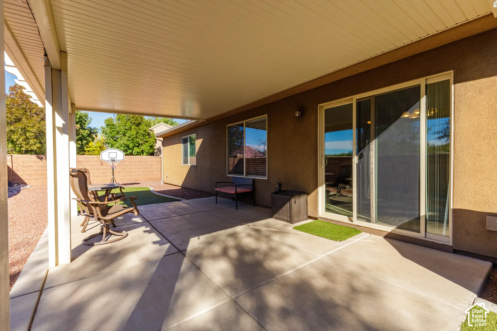 Covered concrete patio featuring a stucco exterior, sliding glass door, and a perimeter masonry wall