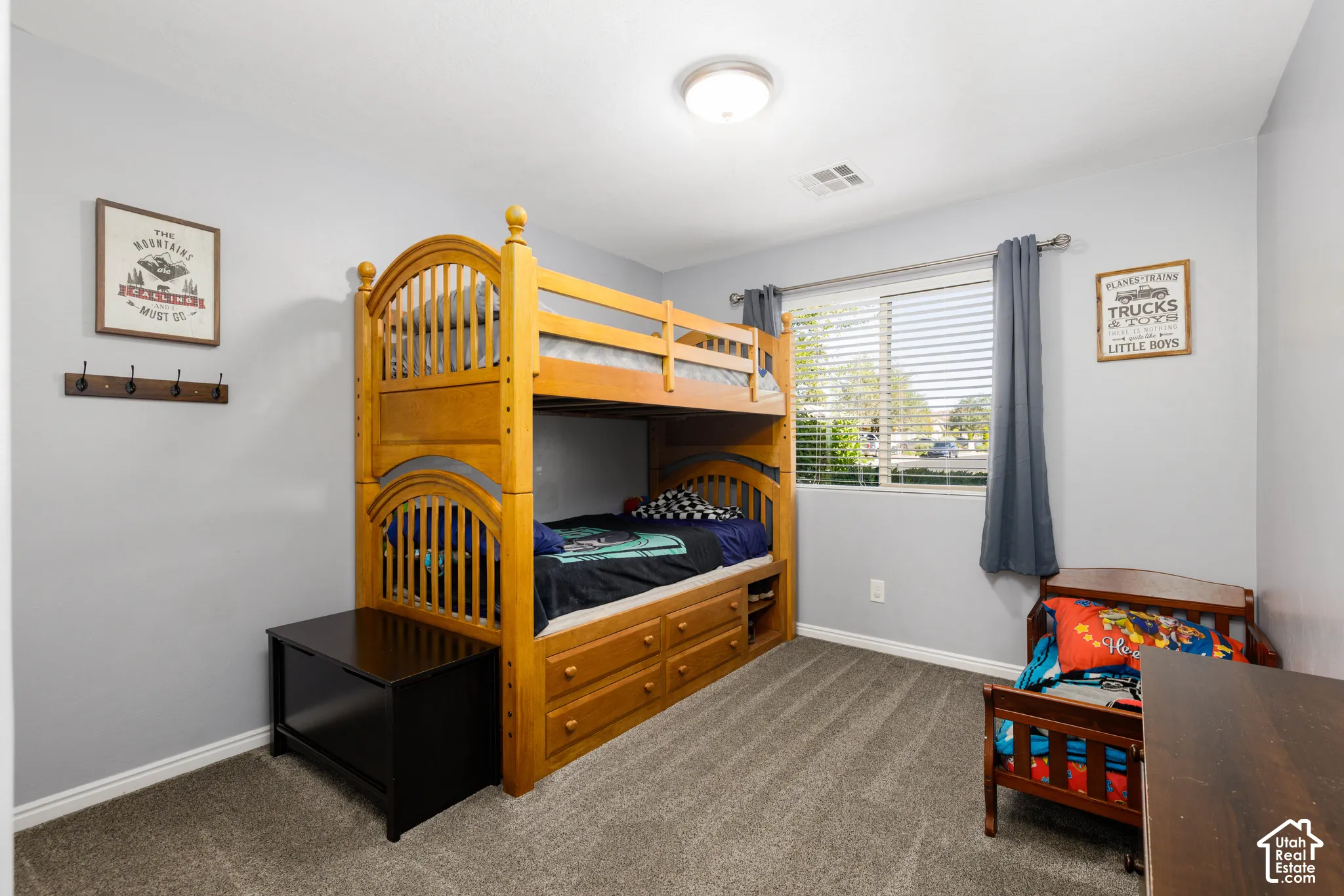 Neutral-toned interior room featuring wall-to-wall carpeting, a horizontal window with adjustable blinds, a ceiling-mounted light fixture, and a wall-mounted hook rack