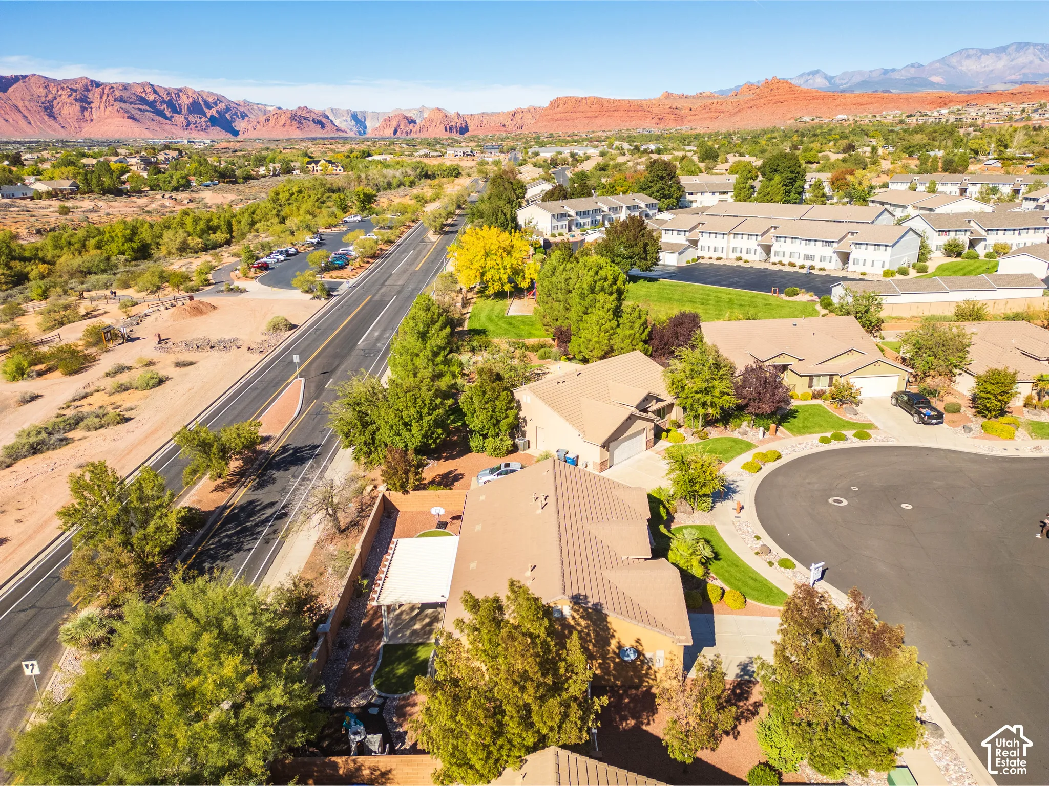 Aerial perspective featuring a tile-roofed residence, concrete driveway, attached garage, private rear patio, and backdrop of red rock mountains